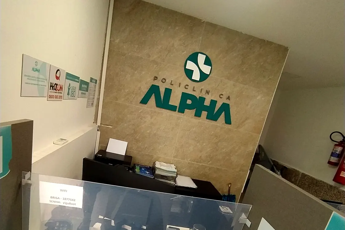 Balcão de atendimento da Policlínica Alpha, com a marca na parede