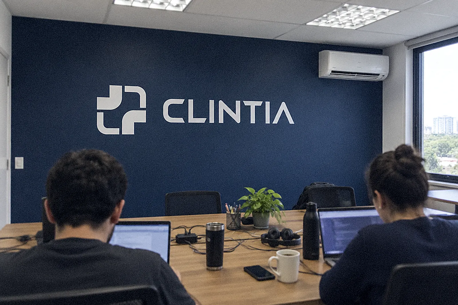 Sala de trabalho com a marca da ClintIA na parede azul e duas pessoas de costas (imagem ilustrativa)